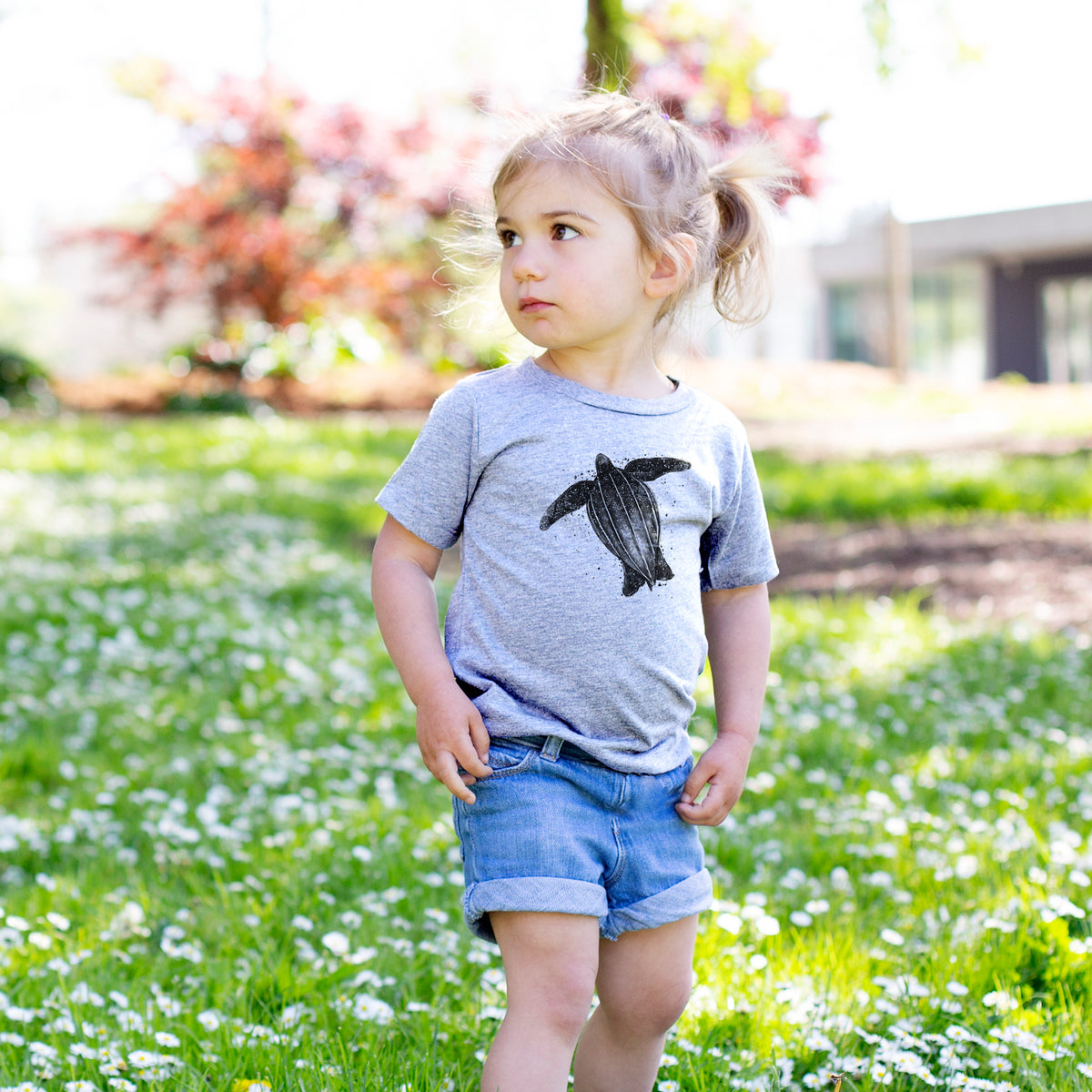 Toddler girl walking outdoors wearing a t-shirt printed with a black ink illustration of a leatherback sea turtle swimming, with ink splatters.