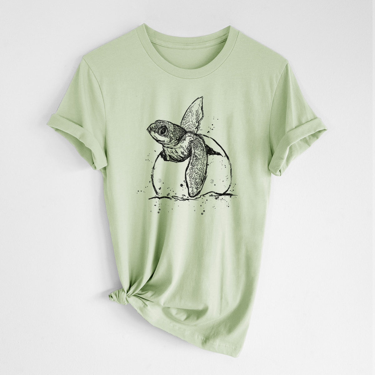 Spring green lightweight cotton t-shirt laid flat with the sleeves rolled, printed with a black ink illustration of a leatherback sea turtle hatchling emerging from its egg.