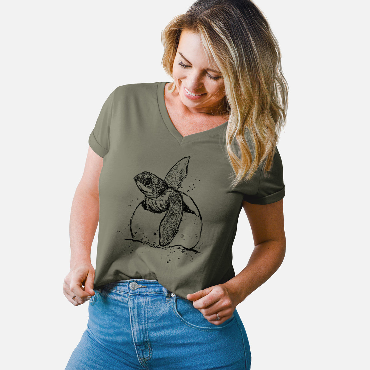 Woman wearing a military green women's relaxed fit cotton V-neck t-shirt printed with a black ink illustration of a leatherback sea turtle hatchling emerging from its egg.