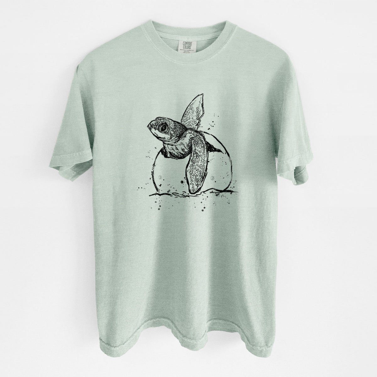 Bay green Comfort Colors t-shirt laid flat, printed with a black ink illustration of a leatherback sea turtle hatchling emerging from its egg.