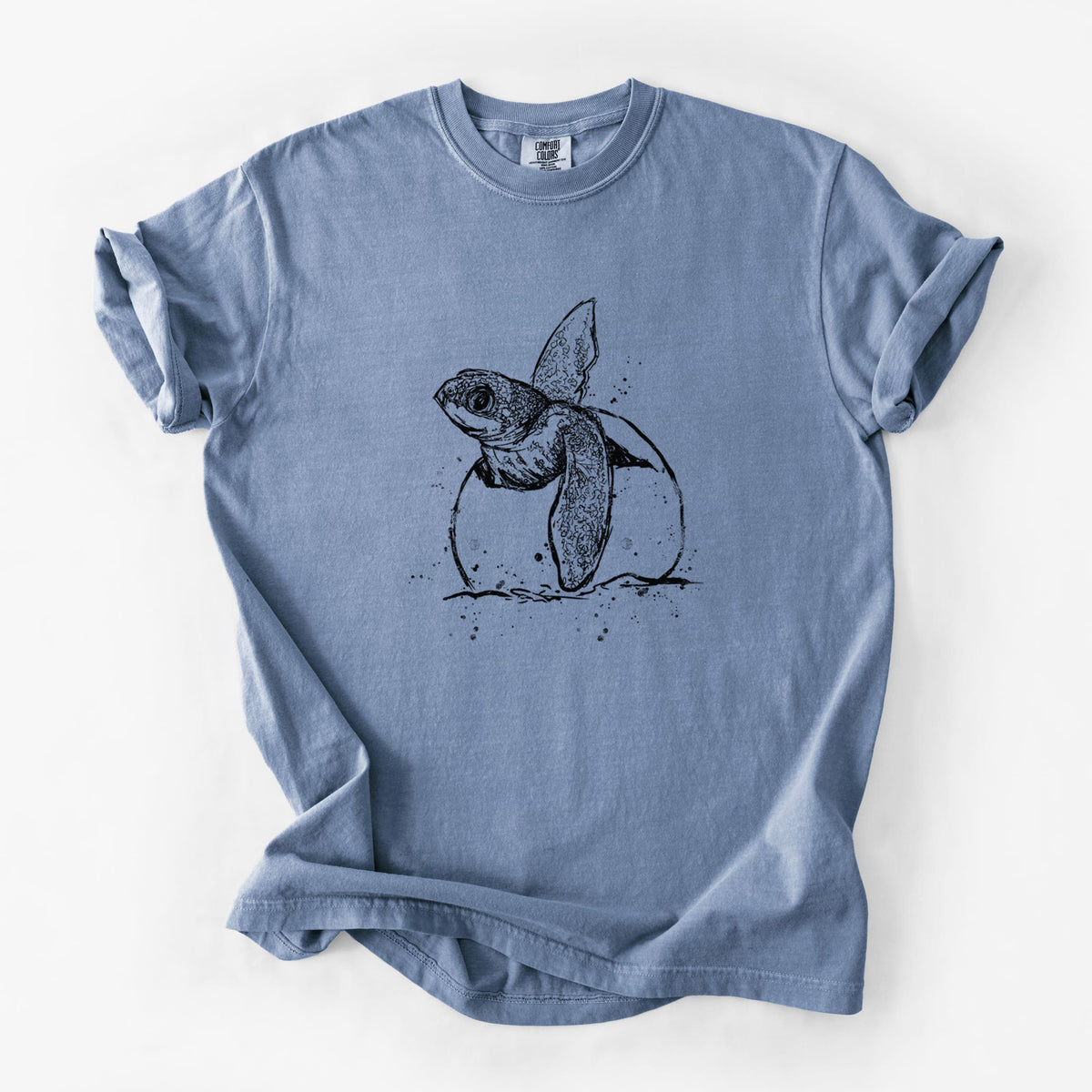 Blue jean Comfort Colors t-shirt laid flat, printed with a black ink illustration of a leatherback sea turtle hatchling emerging from its egg.