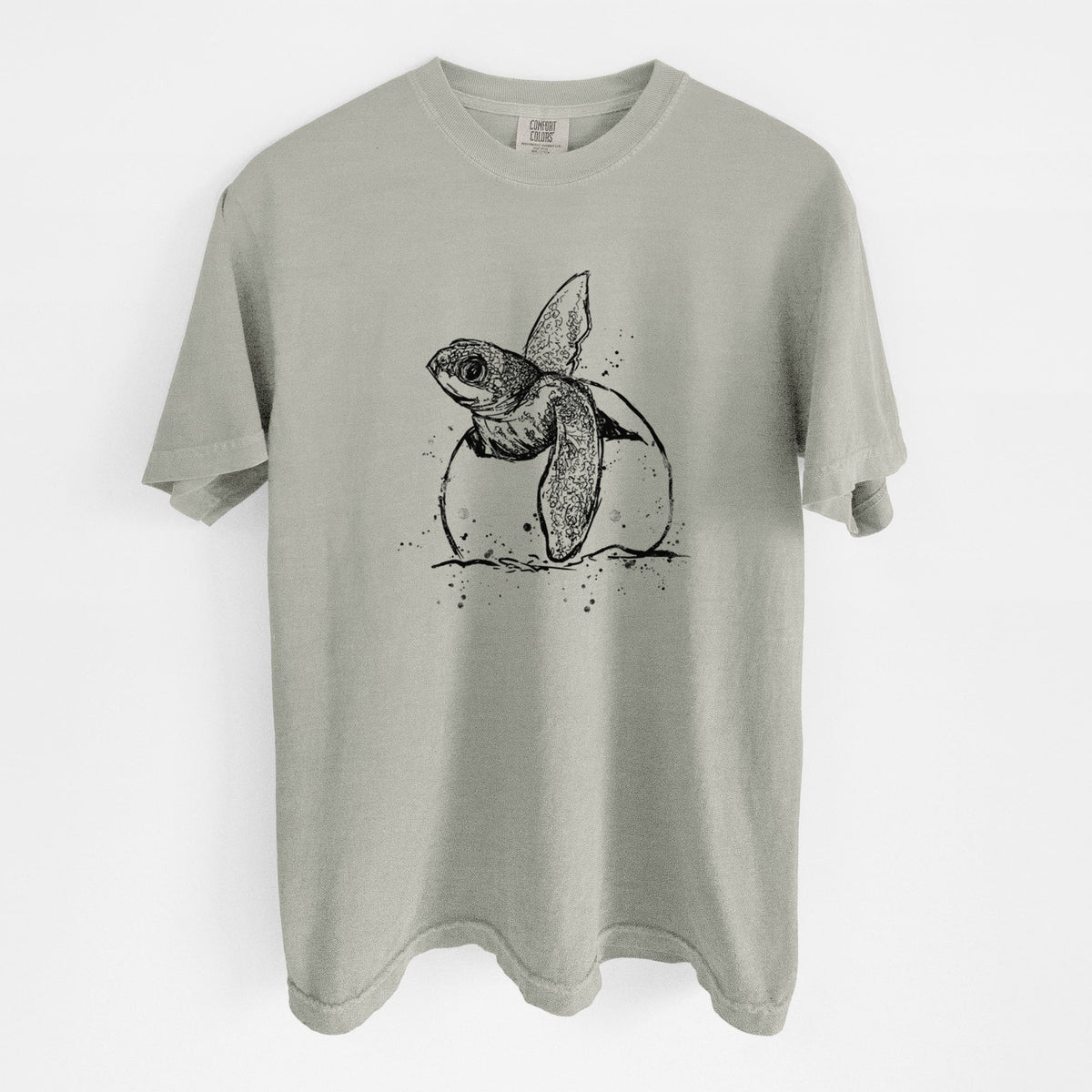 Sandstone beige Comfort Colors t-shirt laid flat, printed with a black ink illustration of a leatherback sea turtle hatchling emerging from its egg.