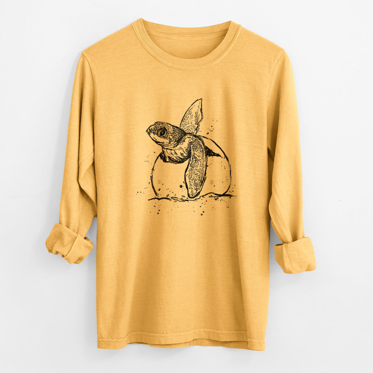 Golden wheat yellow Comfort Colors long sleeve shirt laid flat with the cuffs rolled, printed with a black ink illustration of a leatherback sea turtle hatchling emerging from its egg.