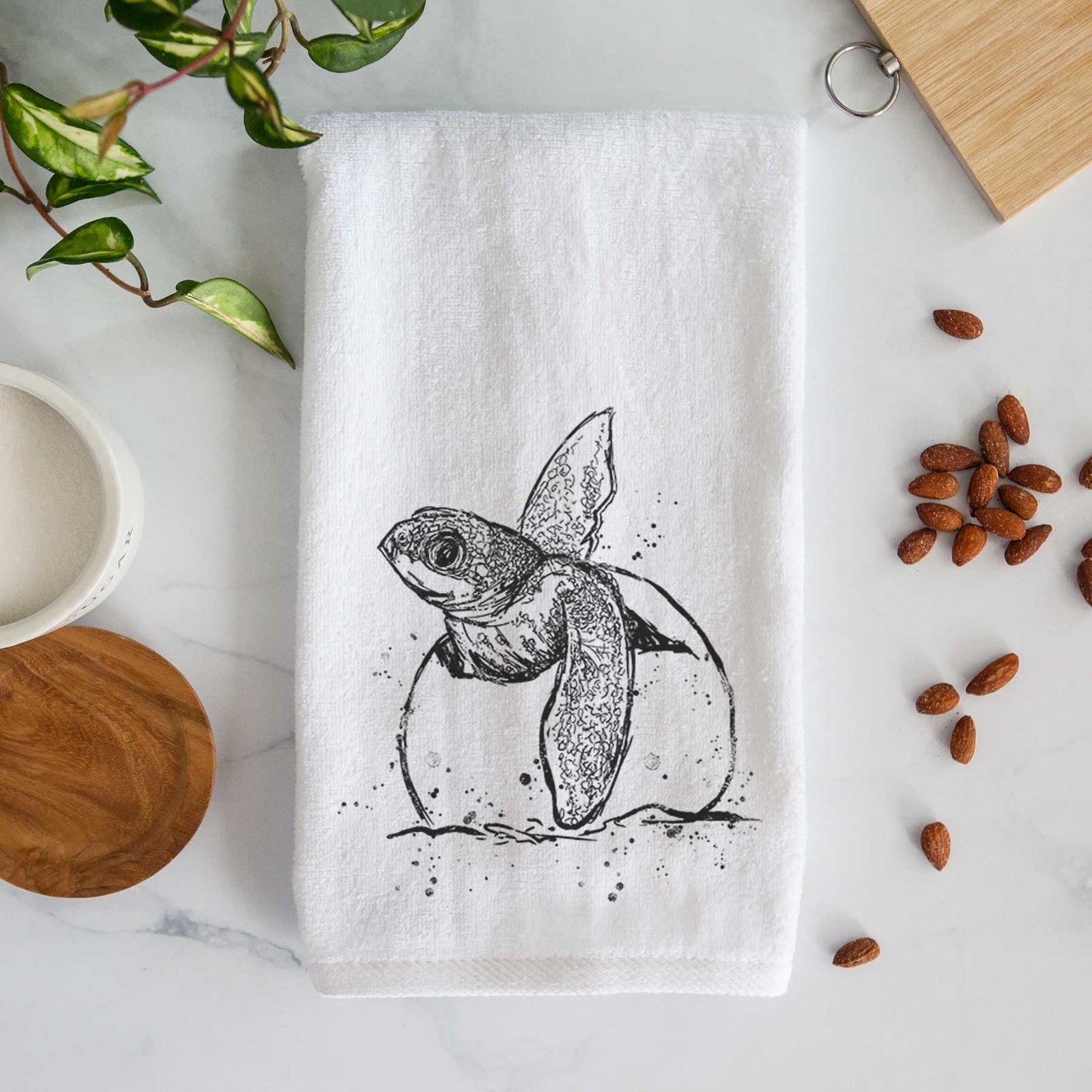 White hand towel printed with a black ink illustration of a leatherback sea turtle hatchling emerging from its egg.