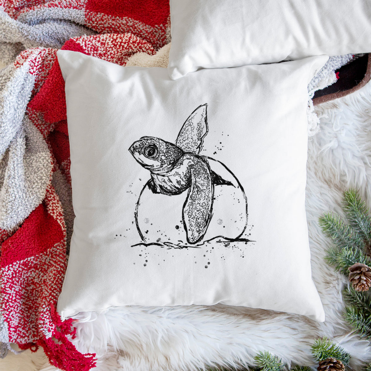 White pillow cover printed with a black ink illustration of a leatherback sea turtle hatchling emerging from its egg, on a woven chair.