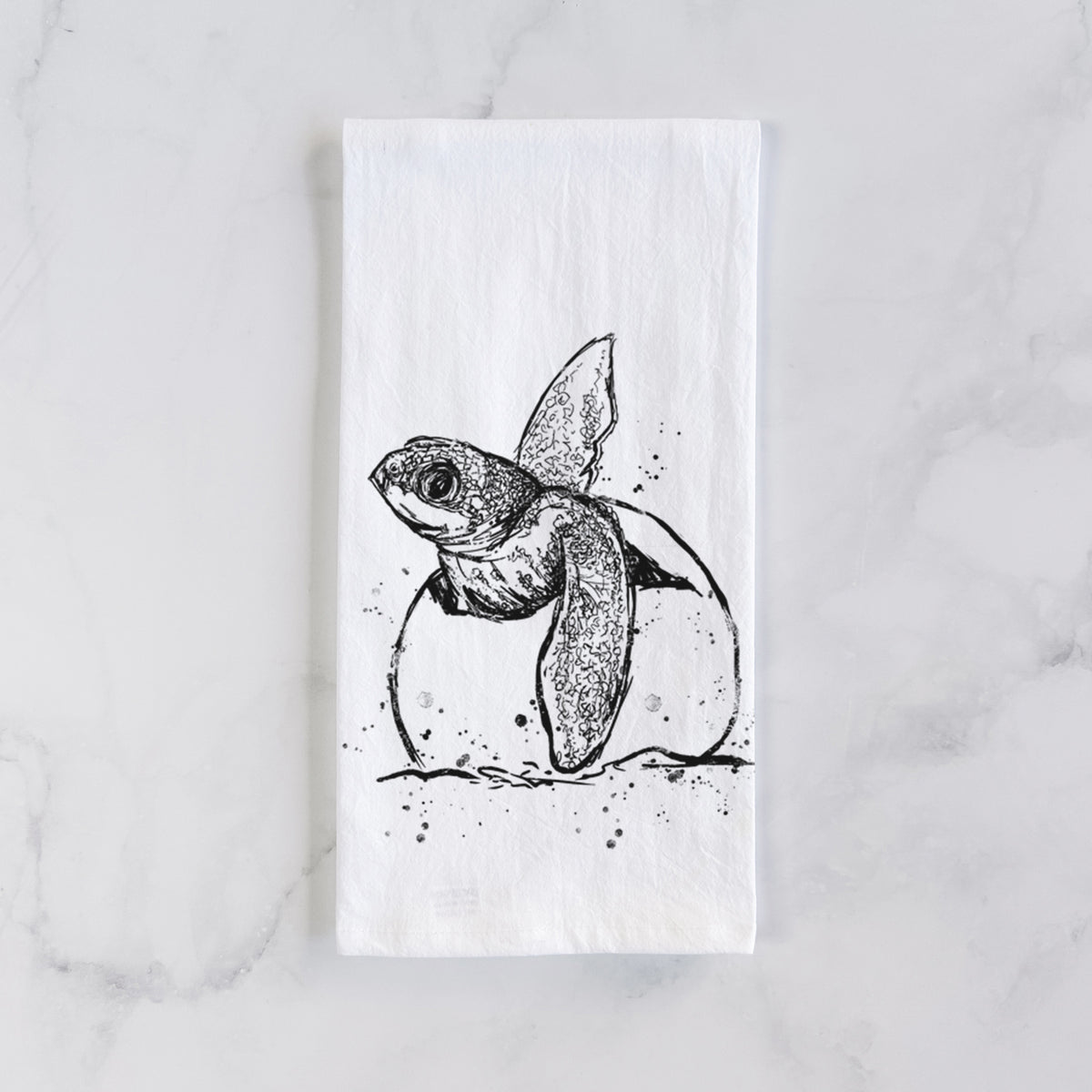 White cotton tea towel laid flat on marble, printed with a black ink illustration of a leatherback sea turtle hatchling emerging from its egg.