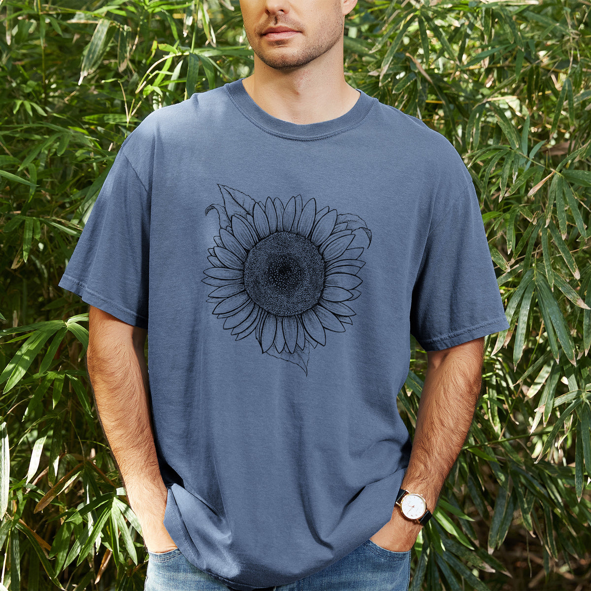 Man wearing a Comfort Colors t-shirt printed with a detailed black ink line drawing of a Lemon Queen sunflower in bloom, outdoors.