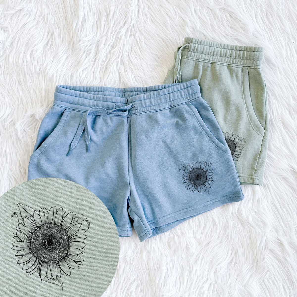 Two pairs of Cali Wave shorts in different colors printed with a detailed black ink line drawing of a Lemon Queen sunflower in bloom, with a close-up of the print.