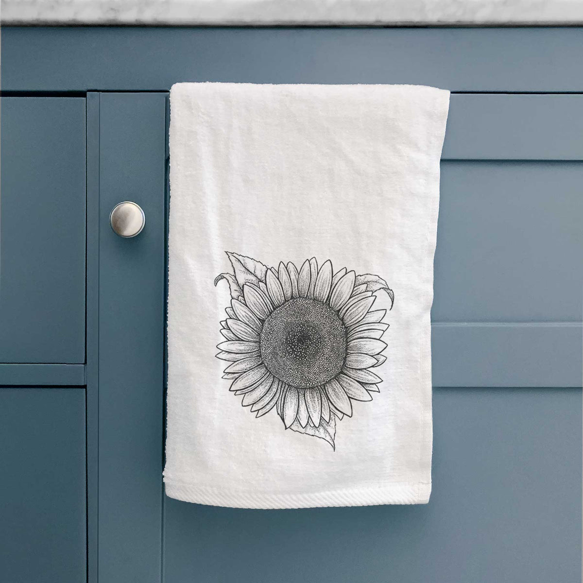 White hand towel printed with a detailed black ink line drawing of a Lemon Queen sunflower in bloom, hanging on a cabinet door.
