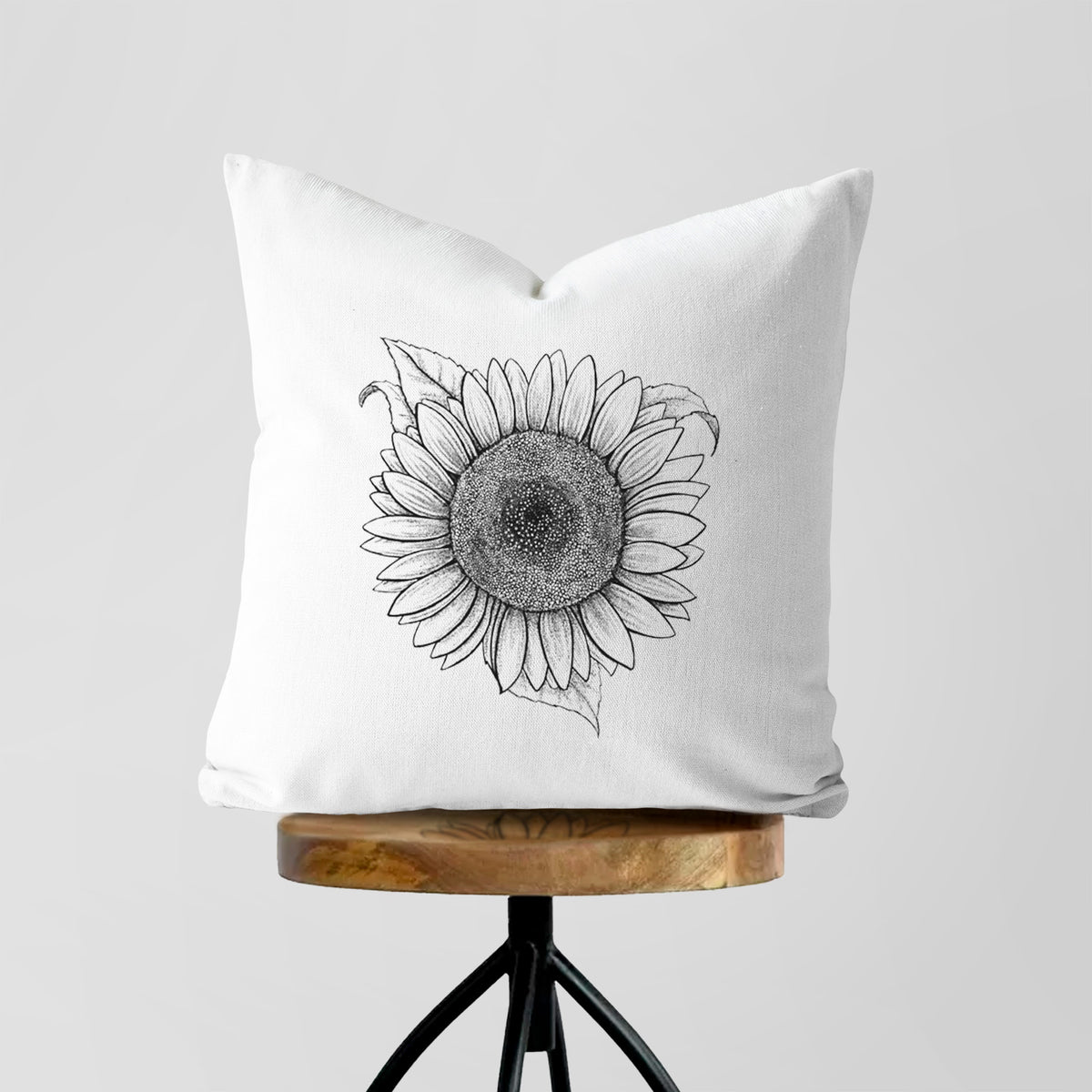 White pillow cover printed with a detailed black ink line drawing of a Lemon Queen sunflower in bloom, on a wooden stool.