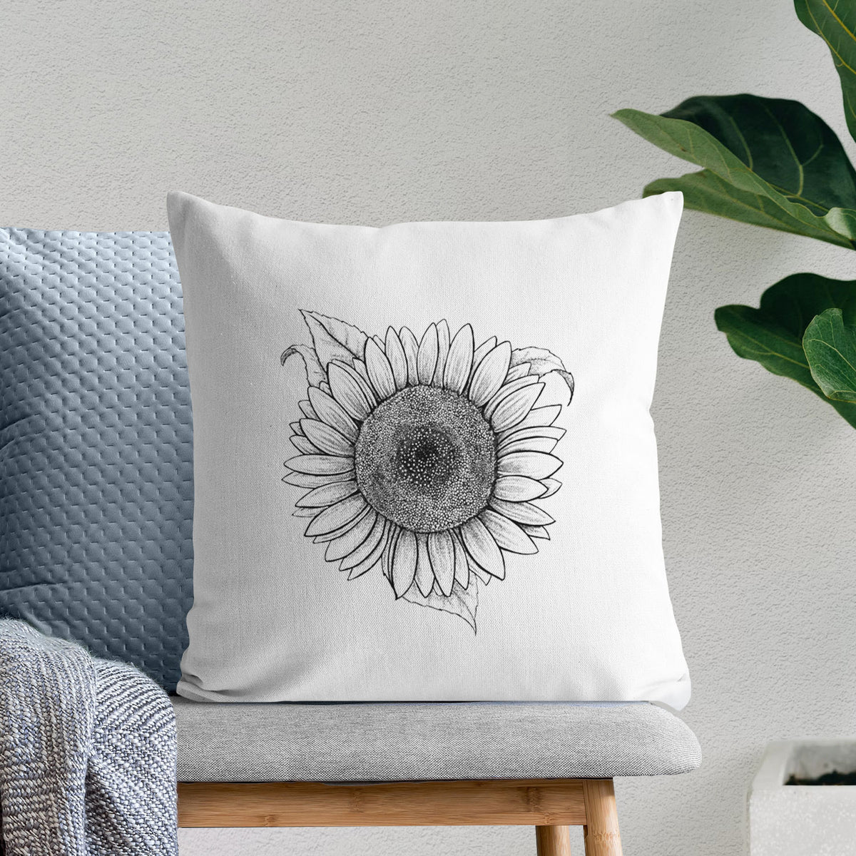 White pillow cover printed with a detailed black ink line drawing of a Lemon Queen sunflower in bloom, on a bench beside plants.