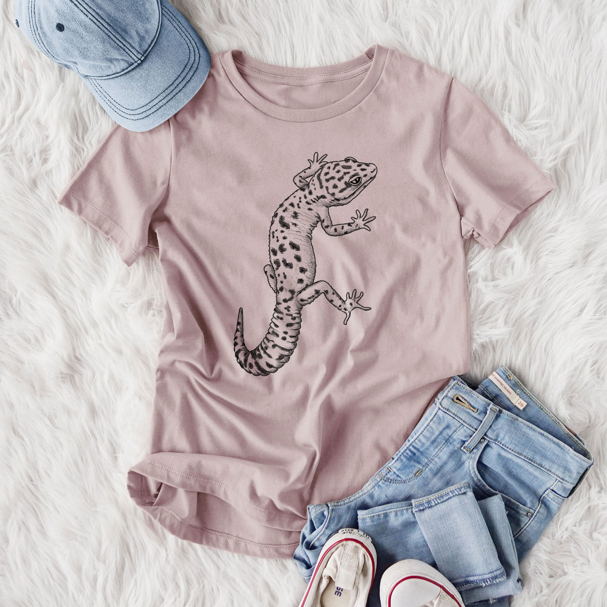 Women's relaxed fit cotton t-shirt printed with a detailed black ink illustration of a spotted leopard gecko climbing, styled flat on a white faux fur rug with jeans.