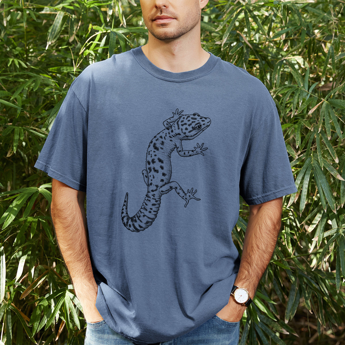 Man wearing a Comfort Colors t-shirt printed with a detailed black ink illustration of a spotted leopard gecko climbing, outdoors.