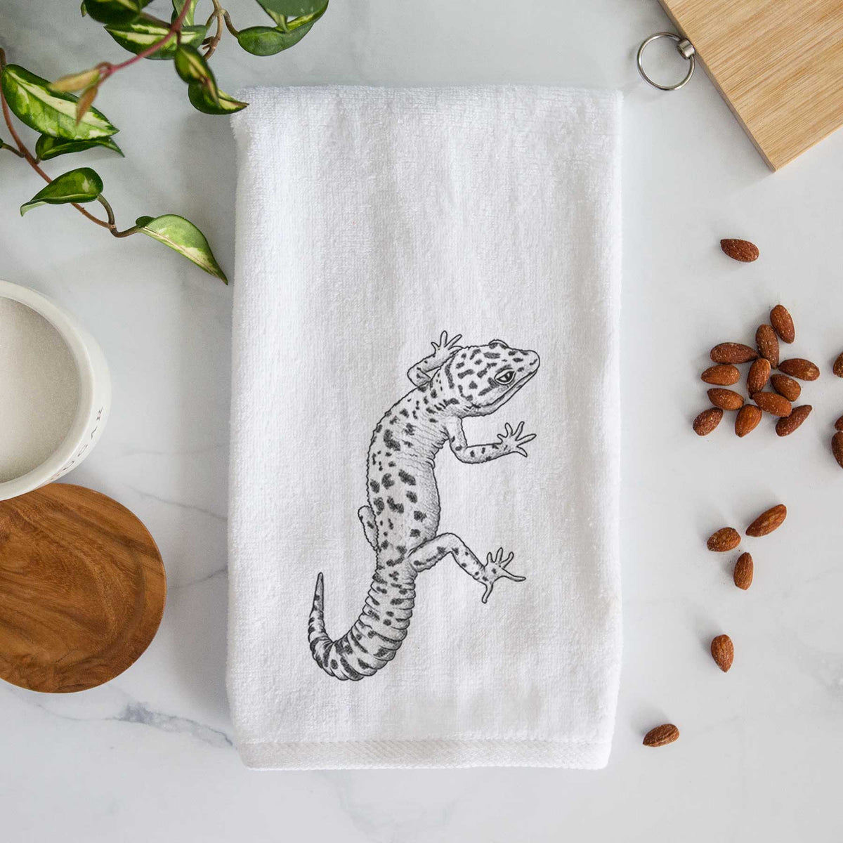 White hand towel printed with a detailed black ink illustration of a spotted leopard gecko climbing.