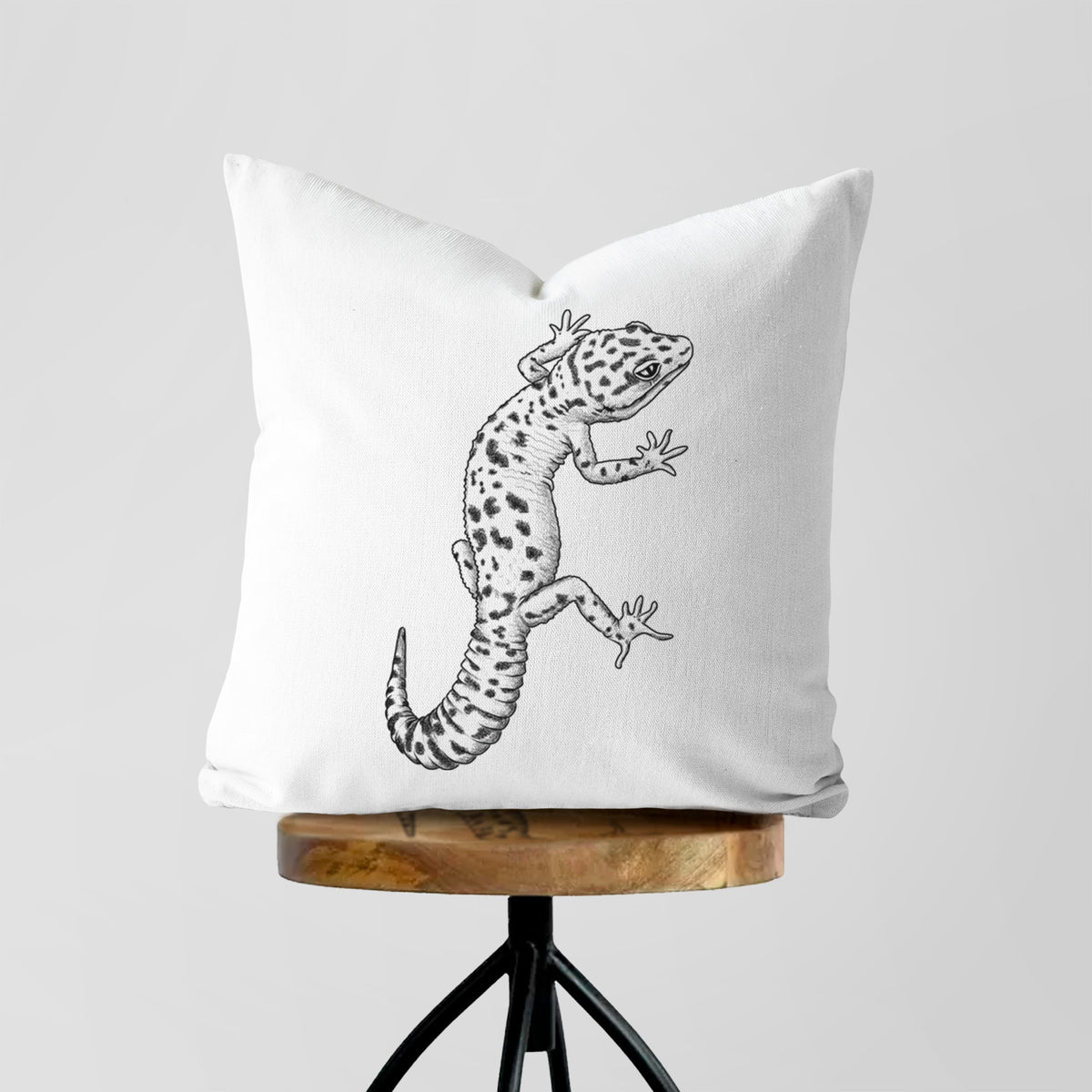 White pillow cover printed with a detailed black ink illustration of a spotted leopard gecko climbing, on a wooden stool.