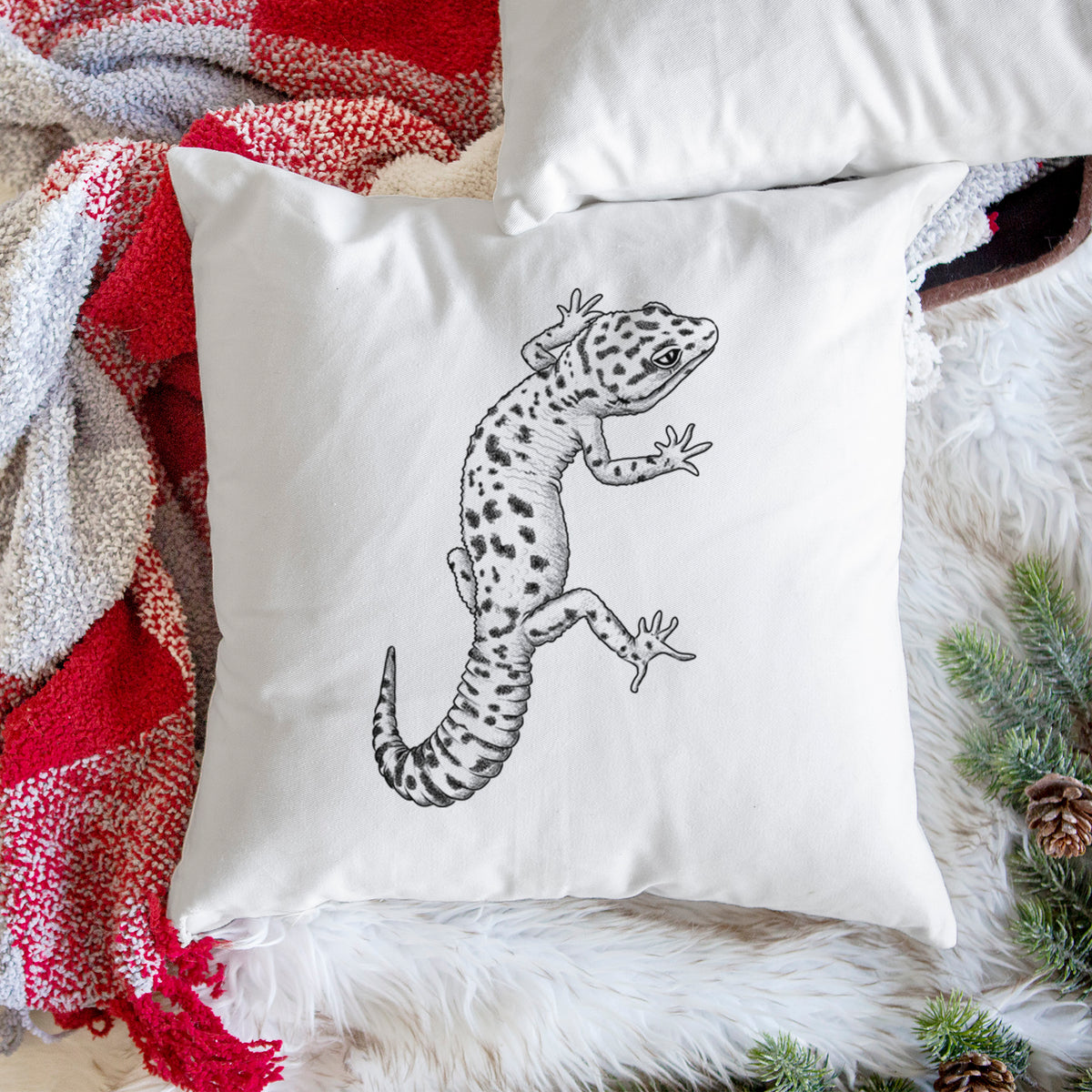 White pillow cover printed with a detailed black ink illustration of a spotted leopard gecko climbing, on a woven chair.