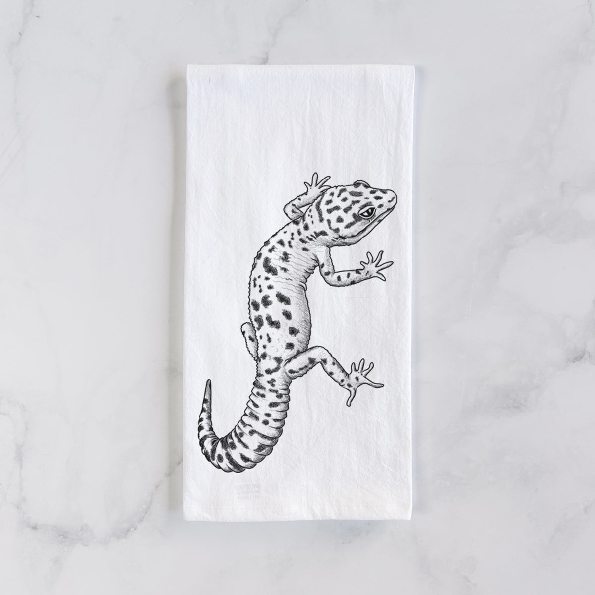 White cotton tea towel laid flat on marble, printed with a detailed black ink illustration of a spotted leopard gecko climbing.