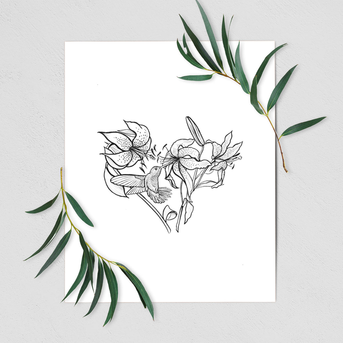 Art print of a black ink line drawing of lilies and a hummingbird arranged in a heart shape, shown with eucalyptus leaves.