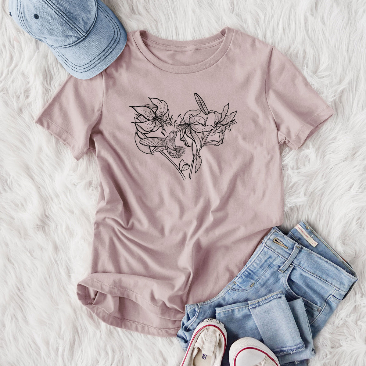 Women's relaxed fit cotton t-shirt printed with a black ink line drawing of lilies and a hummingbird arranged in a heart shape, styled flat on a white faux fur rug with jeans.