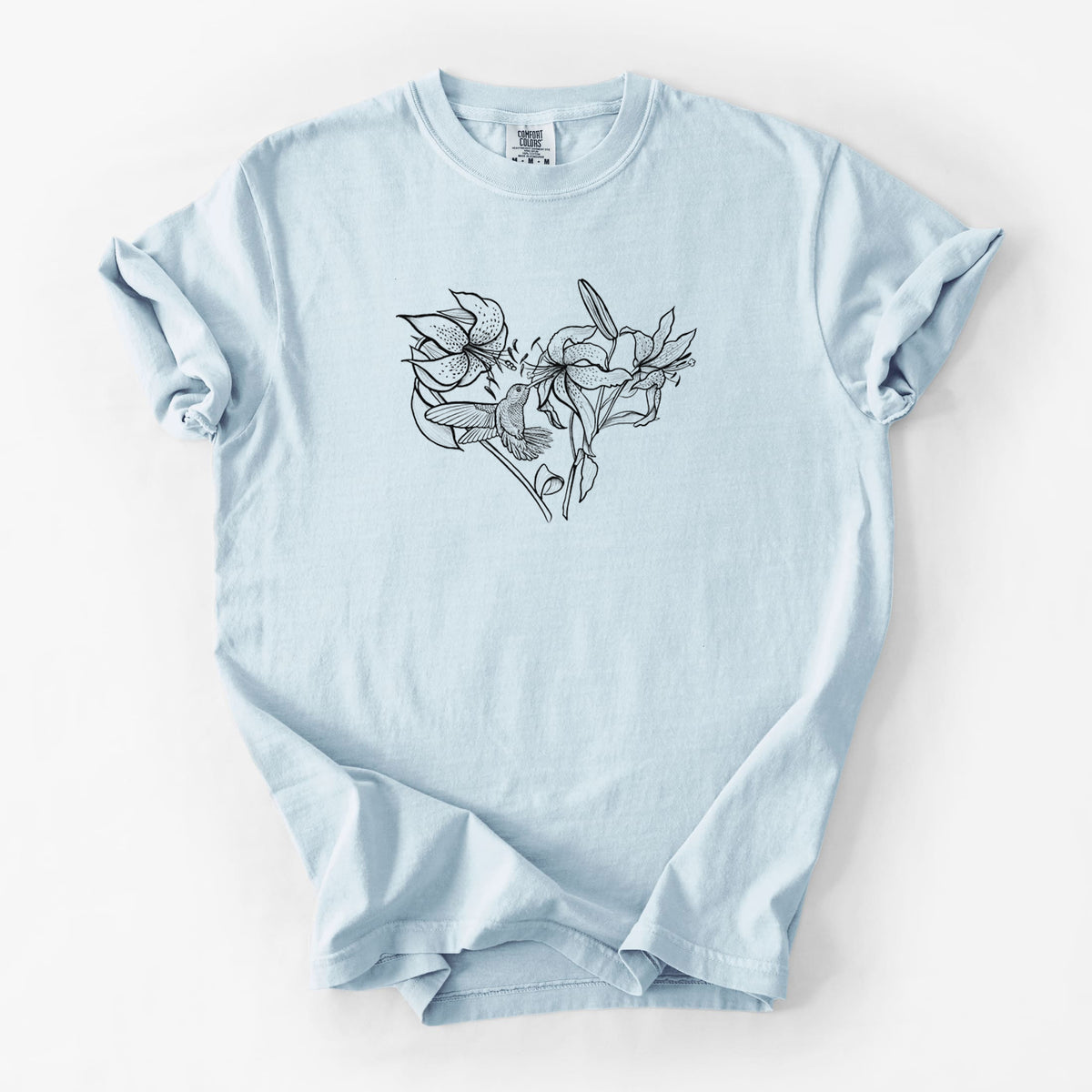 Chambray blue Comfort Colors t-shirt laid flat, printed with a black ink line drawing of lilies and a hummingbird arranged in a heart shape.