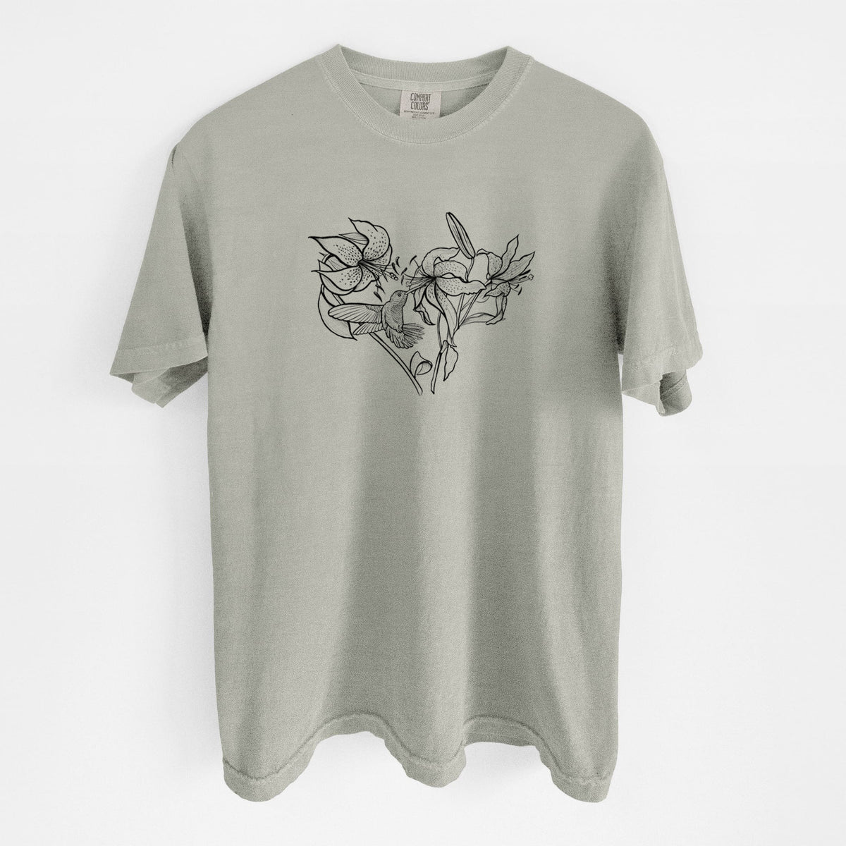 Sandstone beige Comfort Colors t-shirt laid flat, printed with a black ink line drawing of lilies and a hummingbird arranged in a heart shape.
