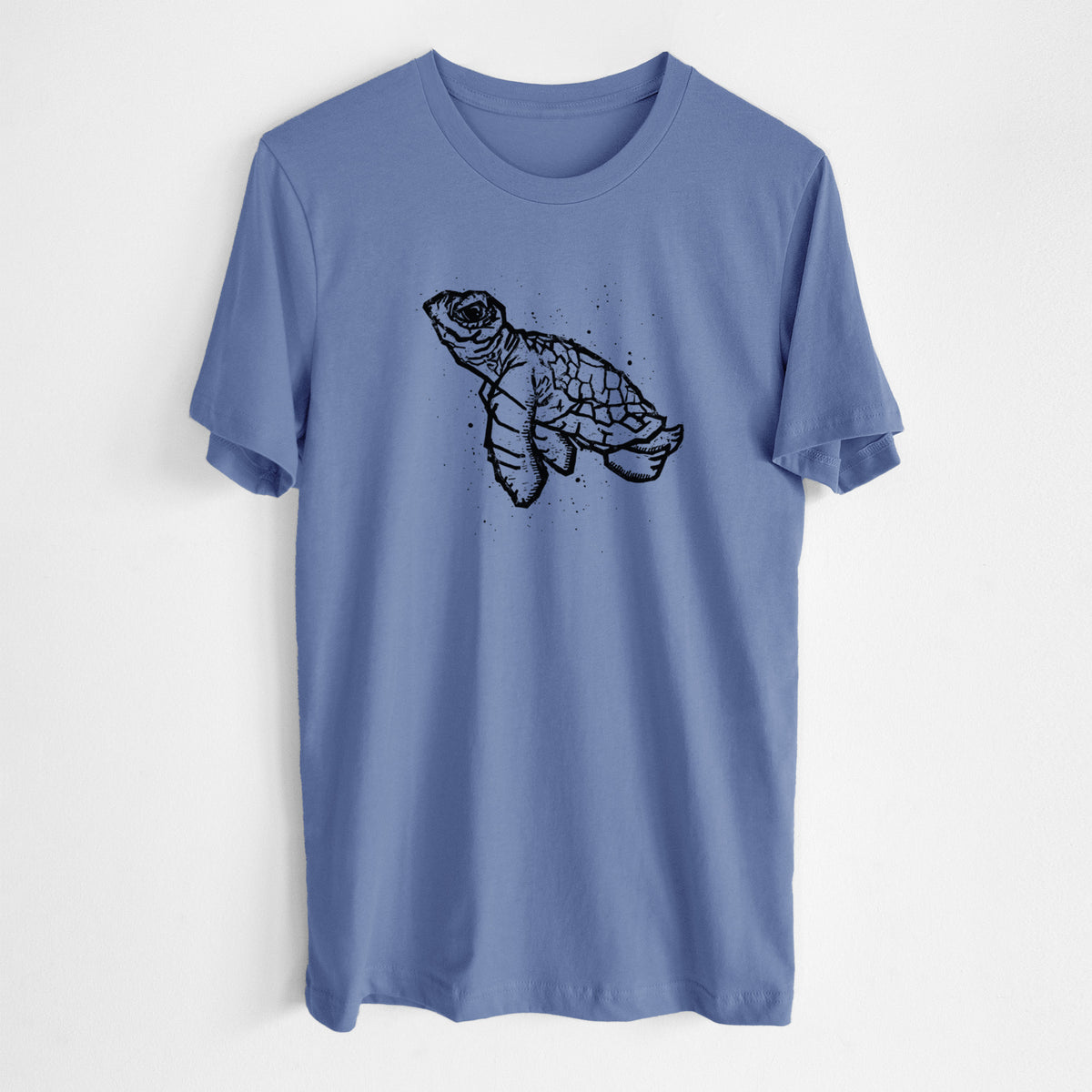Blue bell lightweight cotton t-shirt laid flat, printed with a black linocut-style illustration of a baby sea turtle with a patterned shell and ink splatters.