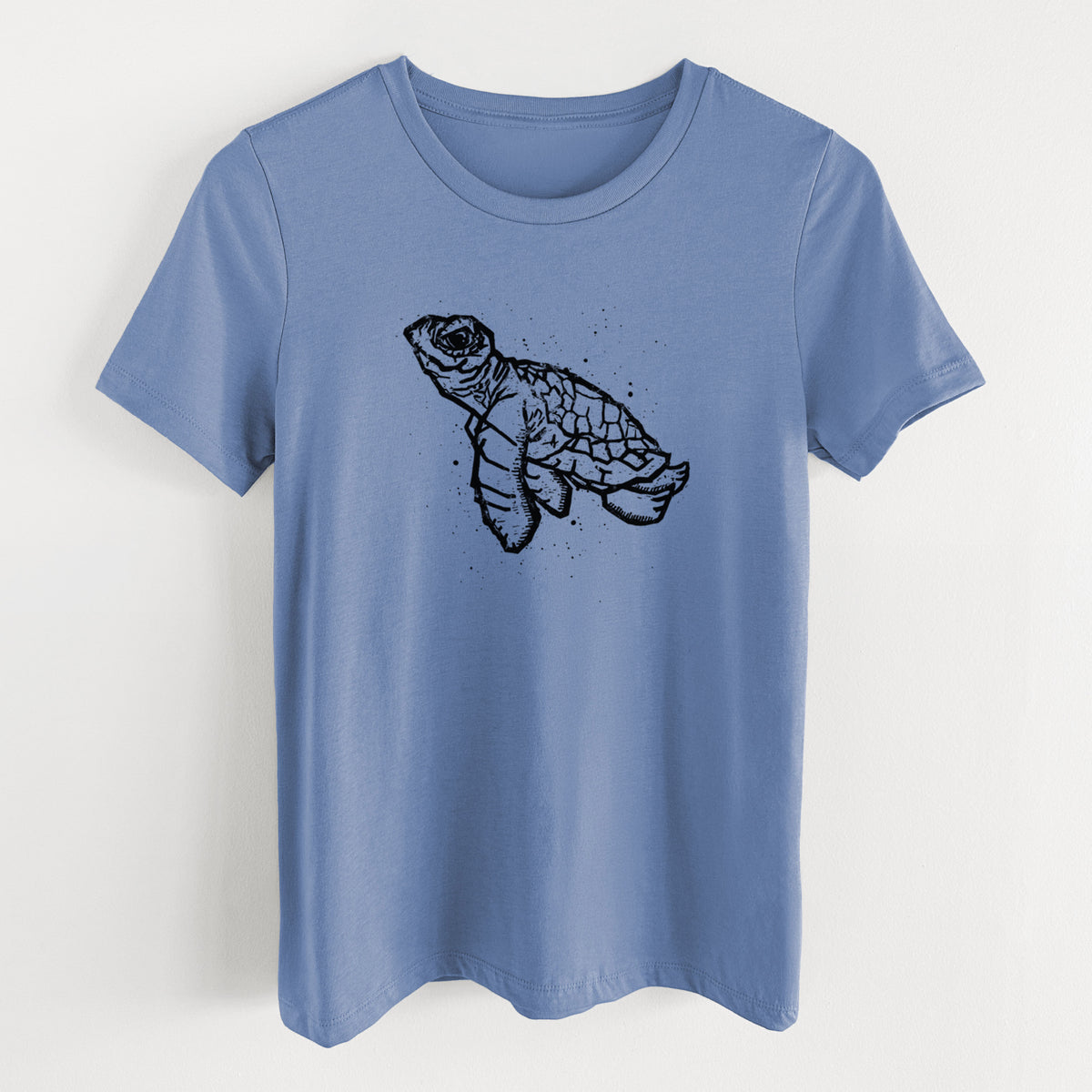 Blue bell women's relaxed fit cotton t-shirt laid flat, printed with a black linocut-style illustration of a baby sea turtle with a patterned shell and ink splatters.
