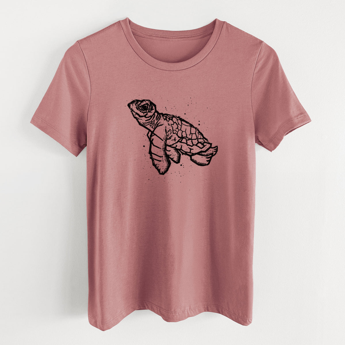 Mauve pink women's relaxed fit cotton t-shirt laid flat, printed with a black linocut-style illustration of a baby sea turtle with a patterned shell and ink splatters.