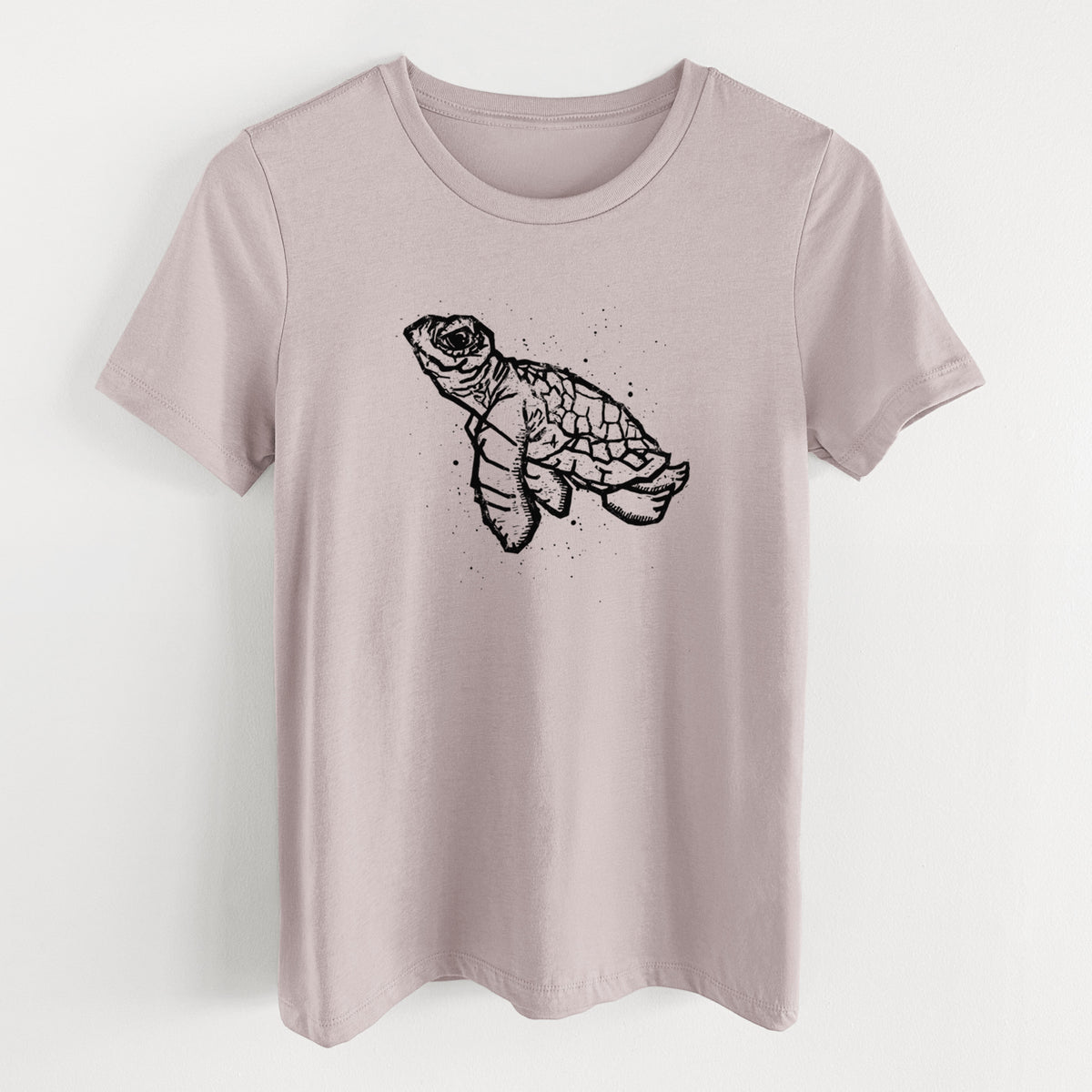 Pink gravel women's relaxed fit cotton t-shirt laid flat, printed with a black linocut-style illustration of a baby sea turtle with a patterned shell and ink splatters.
