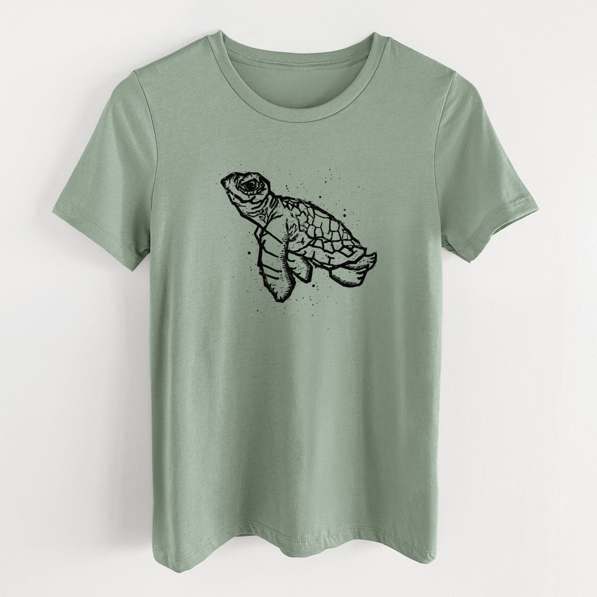 Sage green women's relaxed fit cotton t-shirt laid flat, printed with a black linocut-style illustration of a baby sea turtle with a patterned shell and ink splatters.
