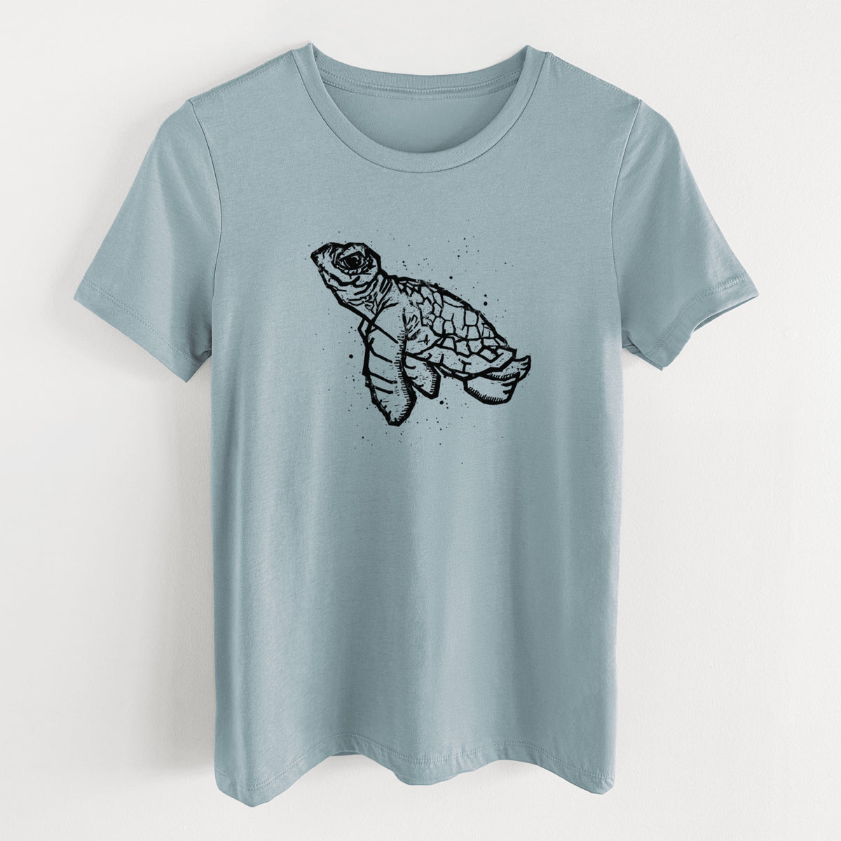 Vintage denim women's relaxed fit cotton t-shirt laid flat, printed with a black linocut-style illustration of a baby sea turtle with a patterned shell and ink splatters.