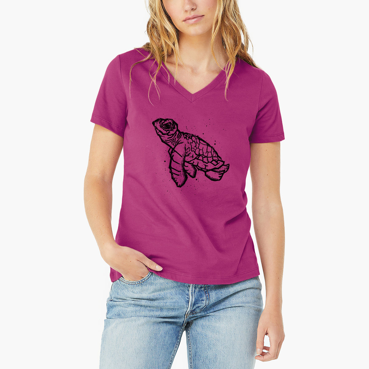 Woman wearing a berry pink women's relaxed fit cotton V-neck t-shirt printed with a black linocut-style illustration of a baby sea turtle with a patterned shell and ink splatters.