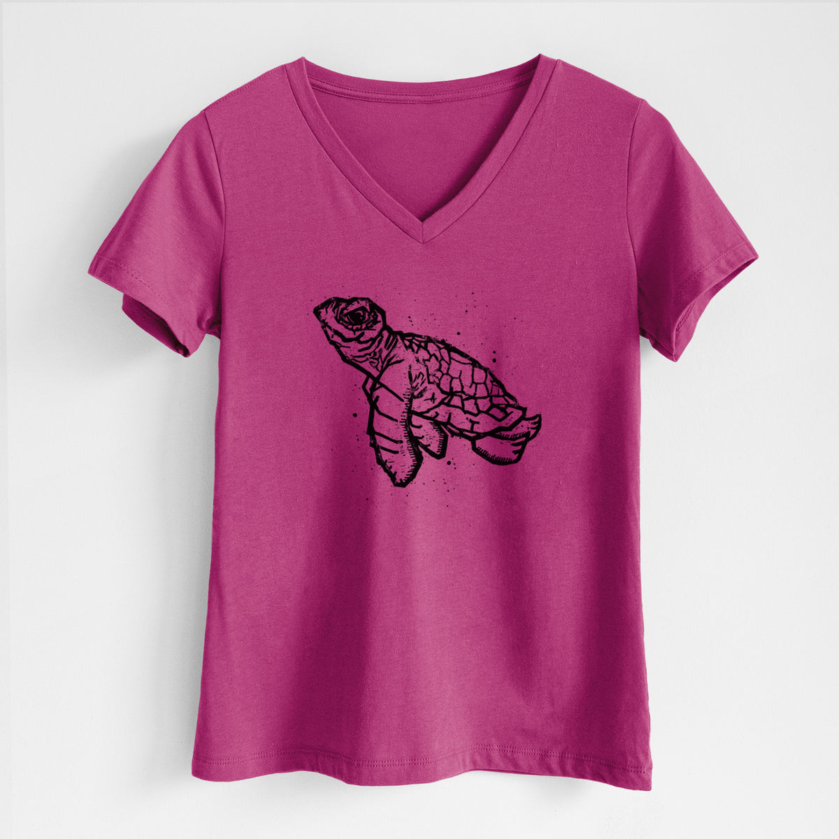 Berry pink women's relaxed fit cotton V-neck t-shirt laid flat, printed with a black linocut-style illustration of a baby sea turtle with a patterned shell and ink splatters.