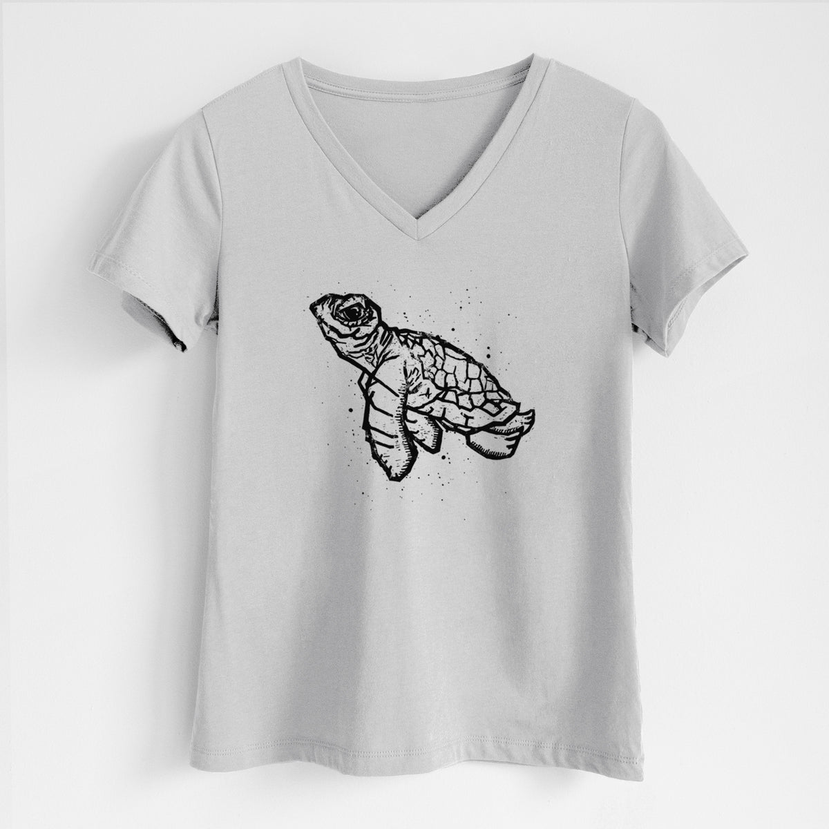 Lunar grey women's relaxed fit cotton V-neck t-shirt laid flat, printed with a black linocut-style illustration of a baby sea turtle with a patterned shell and ink splatters.