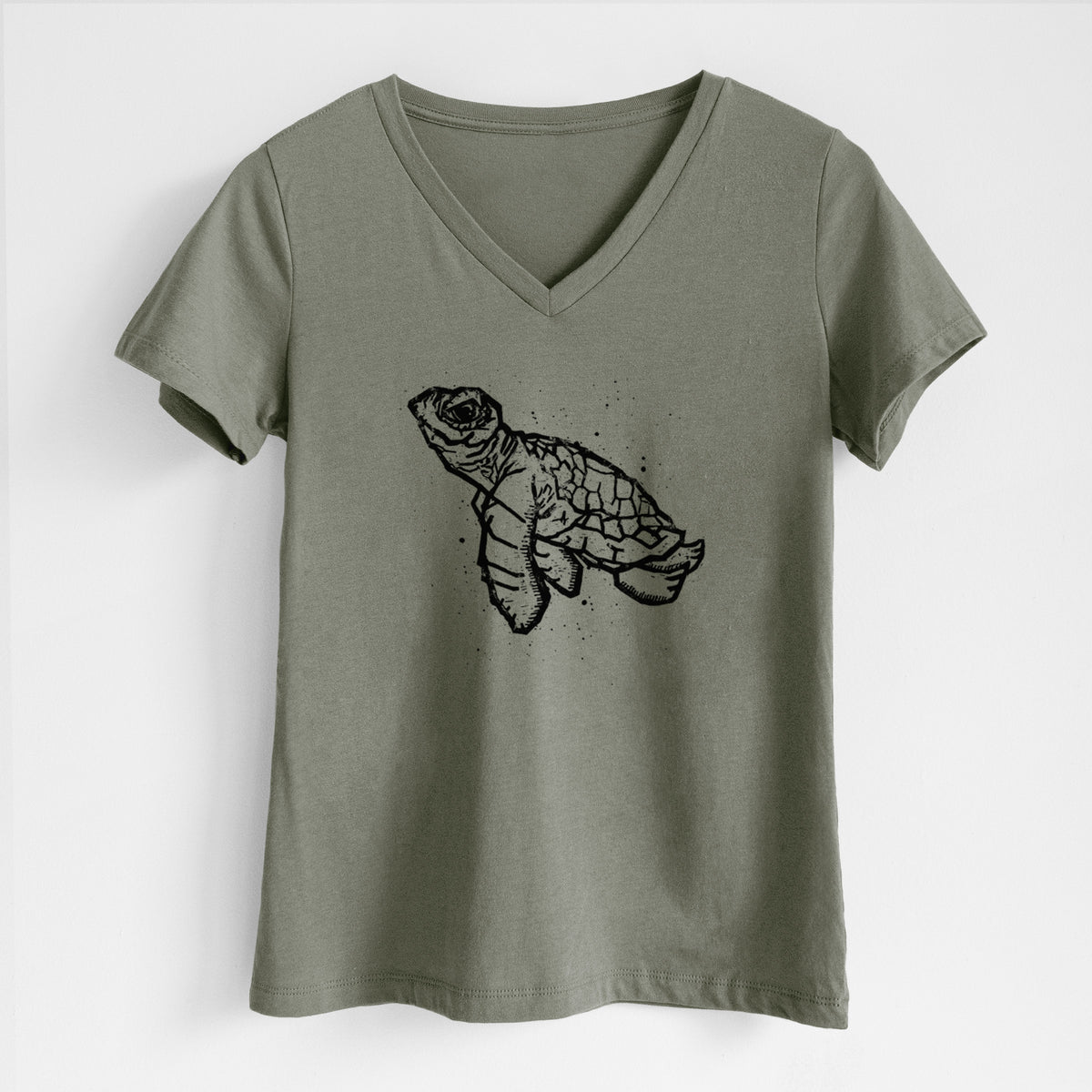 Military green women's relaxed fit cotton V-neck t-shirt laid flat, printed with a black linocut-style illustration of a baby sea turtle with a patterned shell and ink splatters.