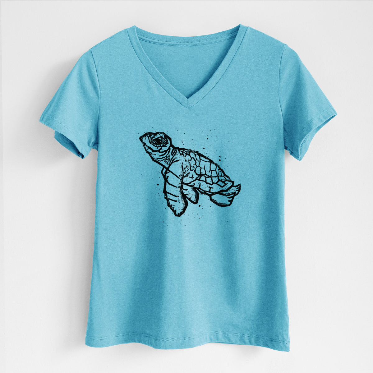 Turquoise women's relaxed fit cotton V-neck t-shirt laid flat, printed with a black linocut-style illustration of a baby sea turtle with a patterned shell and ink splatters.