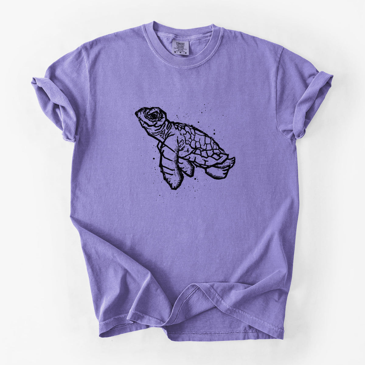 Violet purple Comfort Colors t-shirt laid flat, printed with a black linocut-style illustration of a baby sea turtle with a patterned shell and ink splatters.