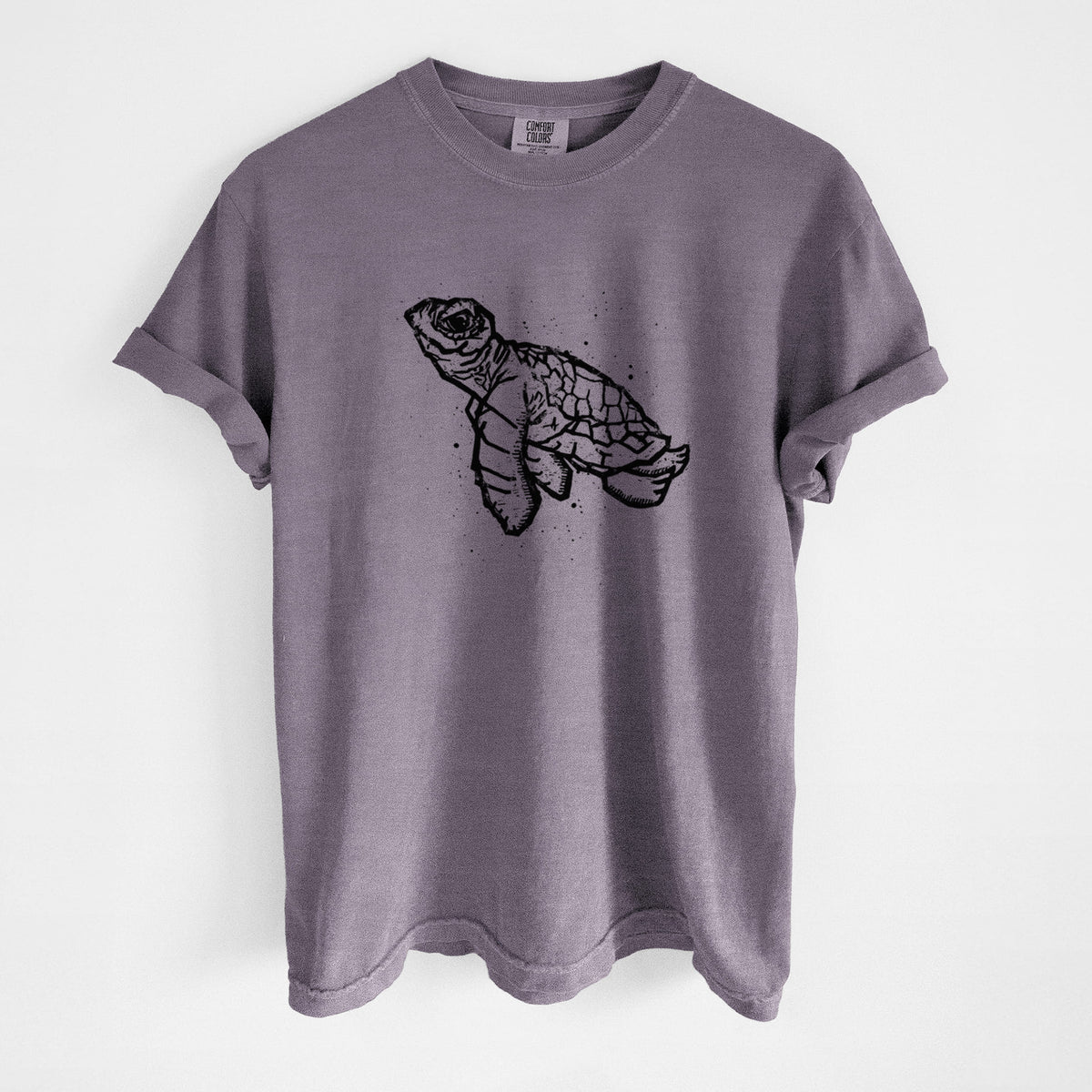 Wine red Comfort Colors t-shirt laid flat, printed with a black linocut-style illustration of a baby sea turtle with a patterned shell and ink splatters.