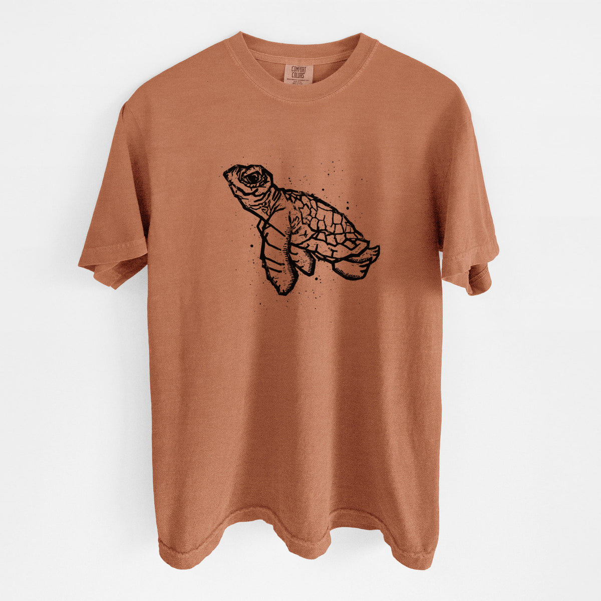 Yam burnt orange Comfort Colors t-shirt laid flat, printed with a black linocut-style illustration of a baby sea turtle with a patterned shell and ink splatters.