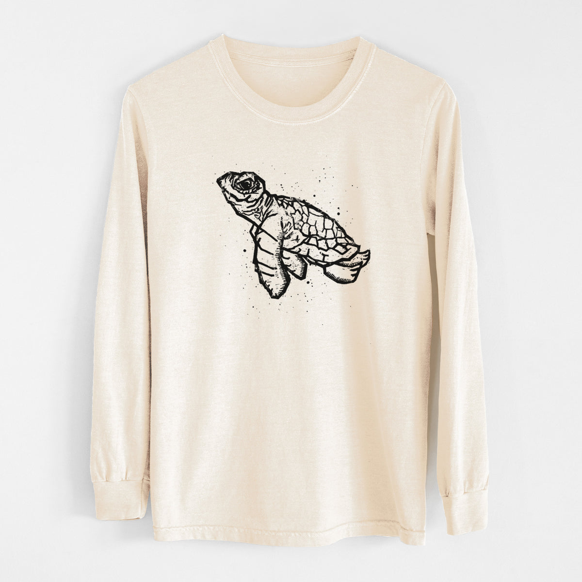 Ivory Comfort Colors long sleeve shirt laid flat, printed with a black linocut-style illustration of a baby sea turtle with a patterned shell and ink splatters.