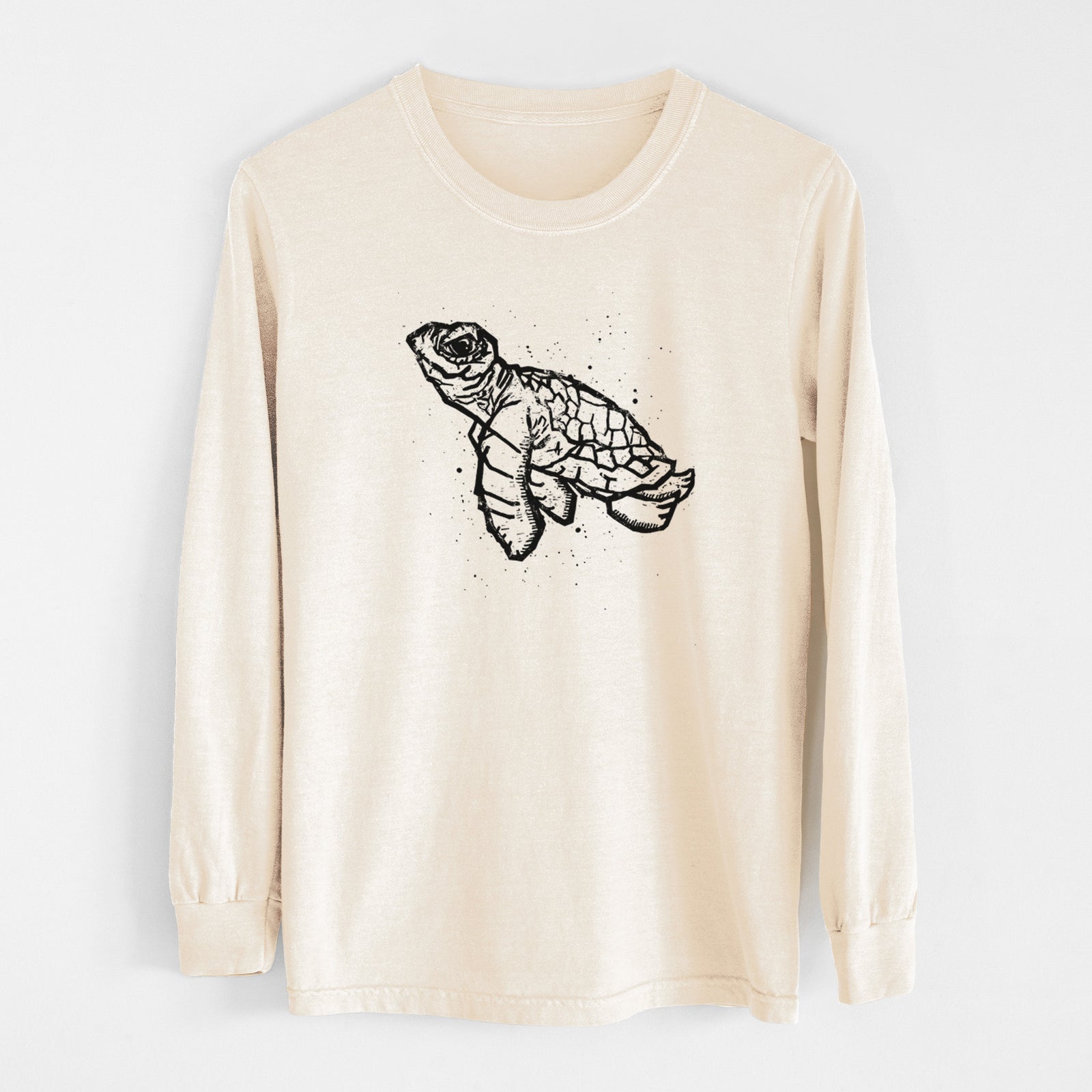 Ivory Comfort Colors long sleeve shirt laid flat, printed with a black linocut-style illustration of a baby sea turtle with a patterned shell and ink splatters.