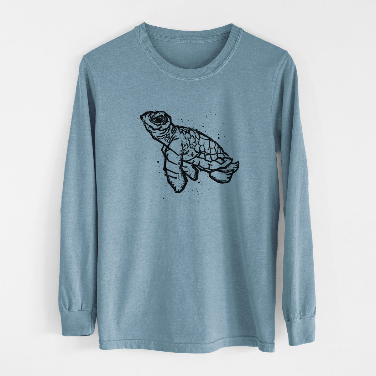 Steel blue Comfort Colors long sleeve shirt laid flat, printed with a black linocut-style illustration of a baby sea turtle with a patterned shell and ink splatters.