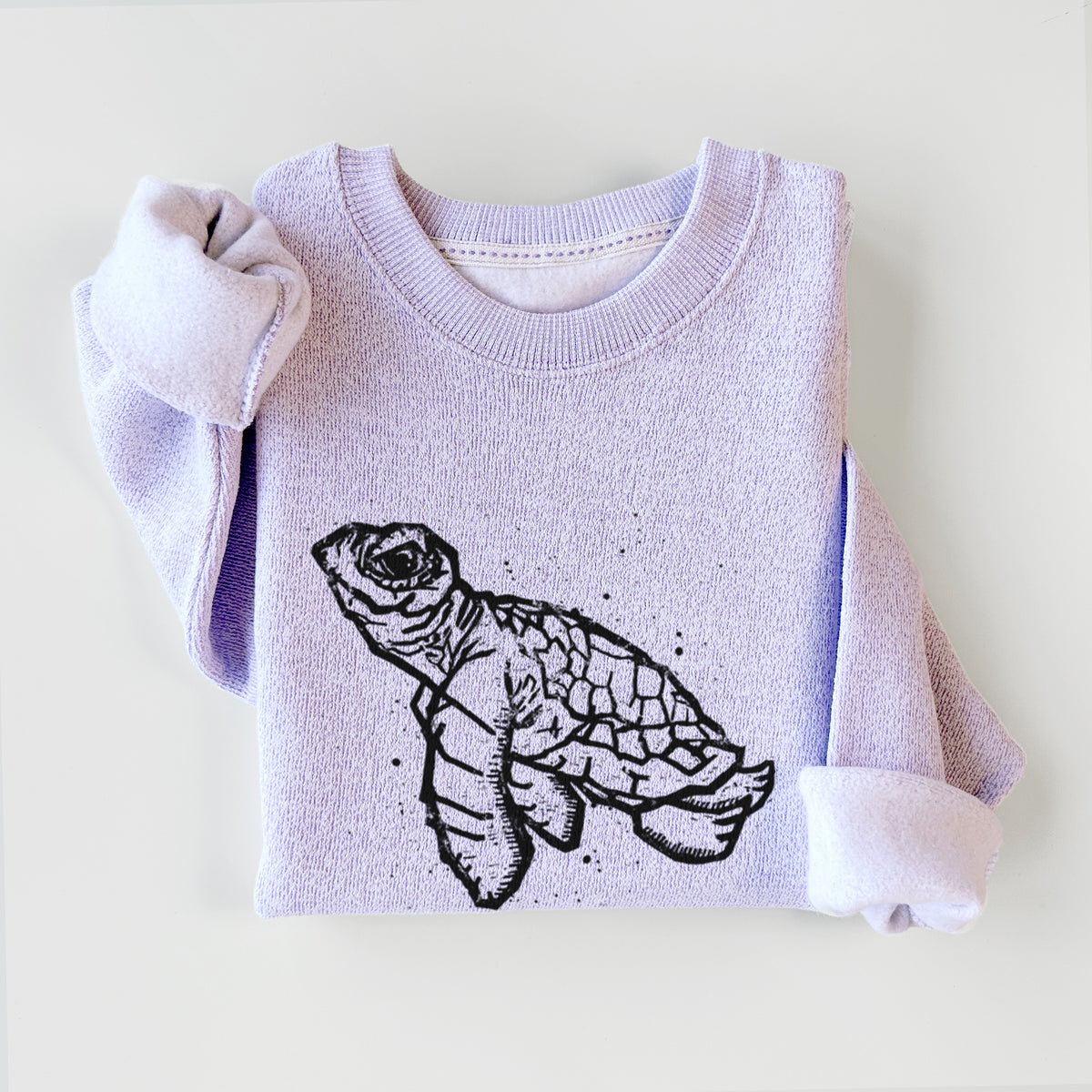 Ice purple knit sweatshirt printed with a black linocut-style illustration of a baby sea turtle with a patterned shell and ink splatters, styled flat.
