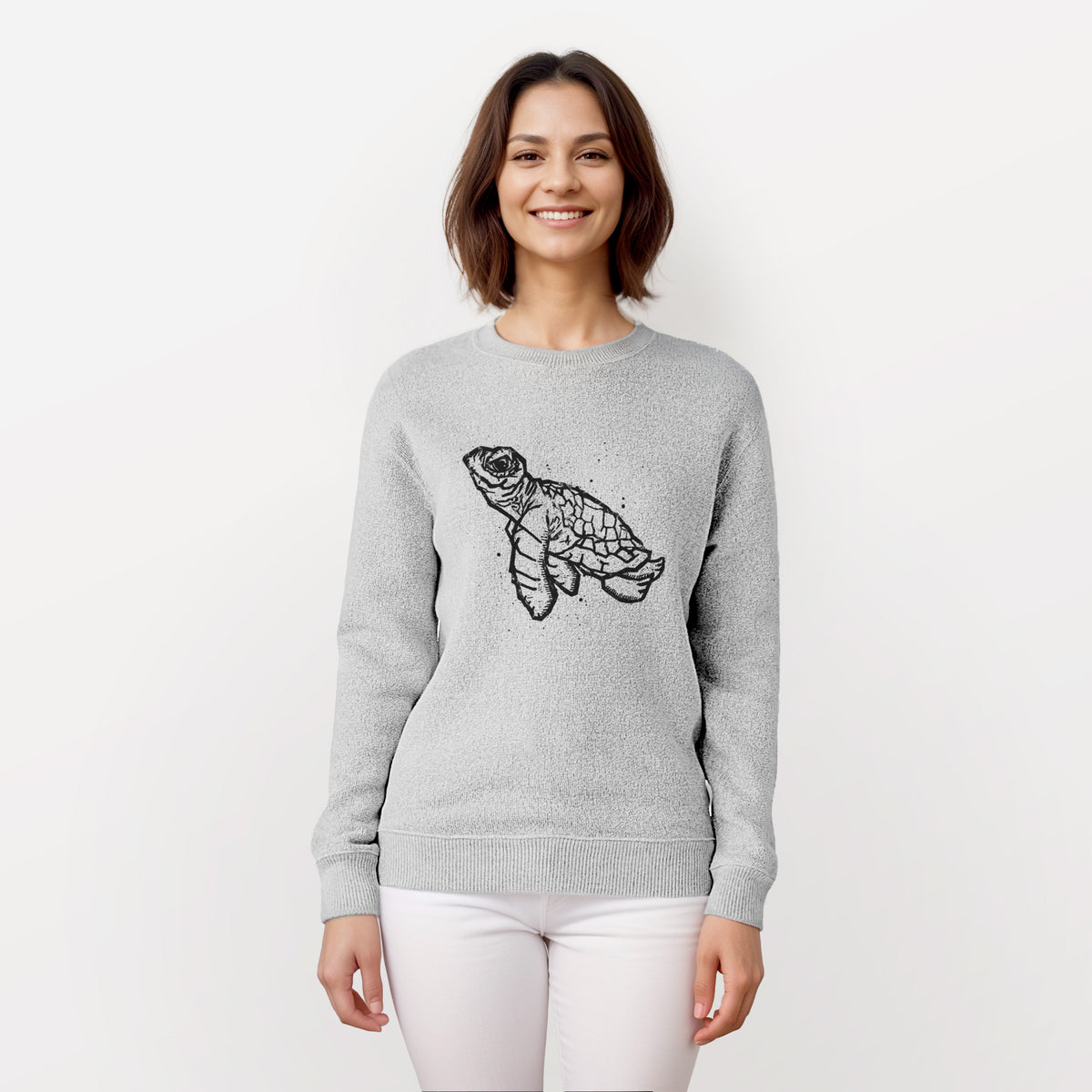 Woman wearing a knit sweatshirt printed with a black linocut-style illustration of a baby sea turtle with a patterned shell and ink splatters.