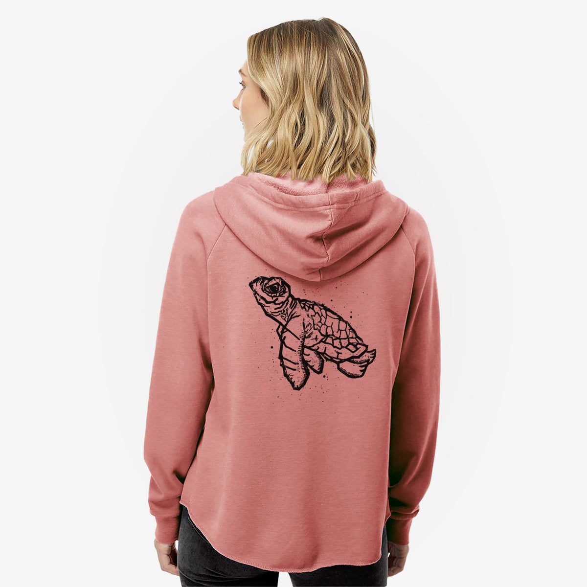Woman wearing a dusty rose women's Cali Wave zip-up sweatshirt printed with a black linocut-style illustration of a baby sea turtle with a patterned shell and ink splatters, seen from behind.