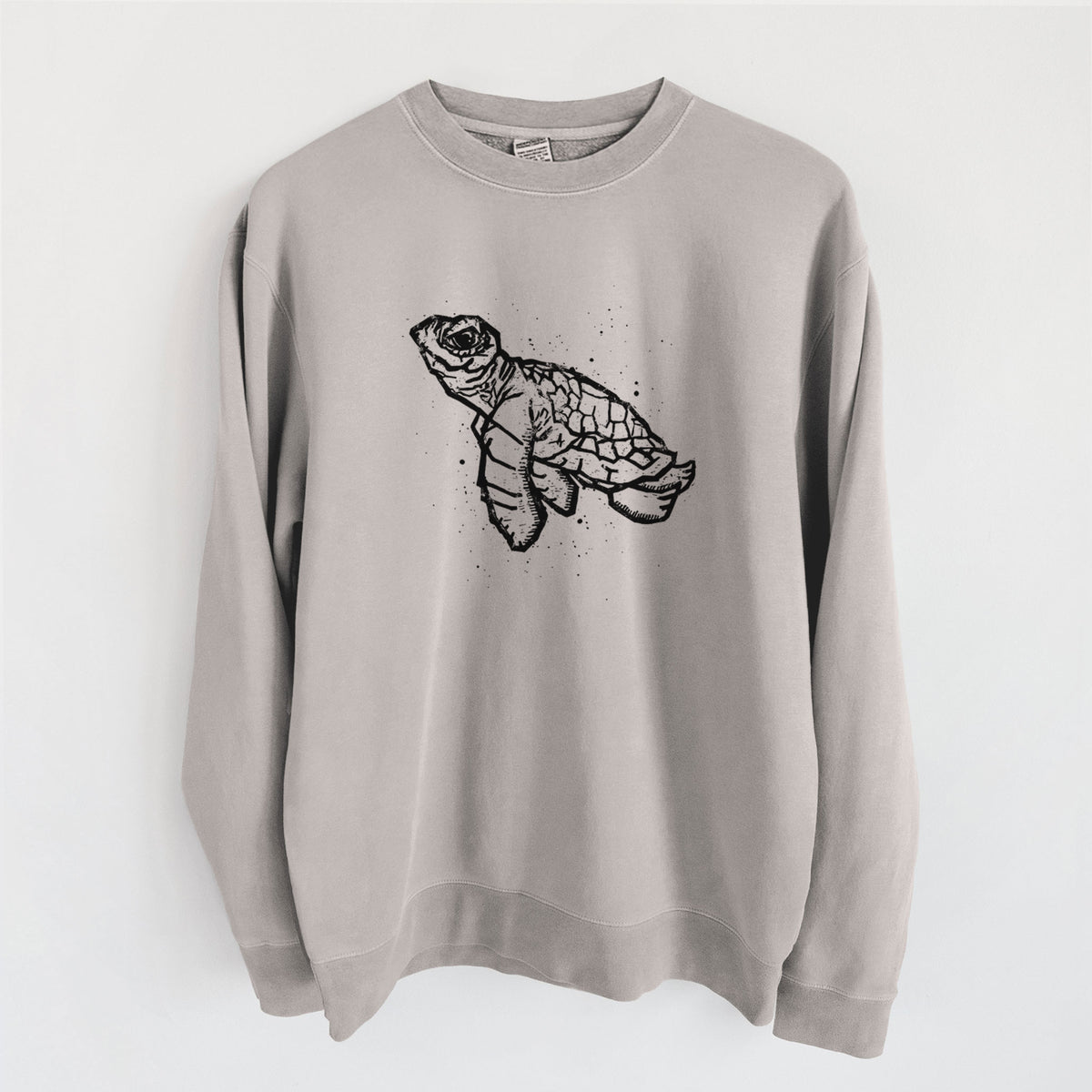 Cement grey pigment dyed crewneck sweatshirt laid flat, printed with a black linocut-style illustration of a baby sea turtle with a patterned shell and ink splatters.