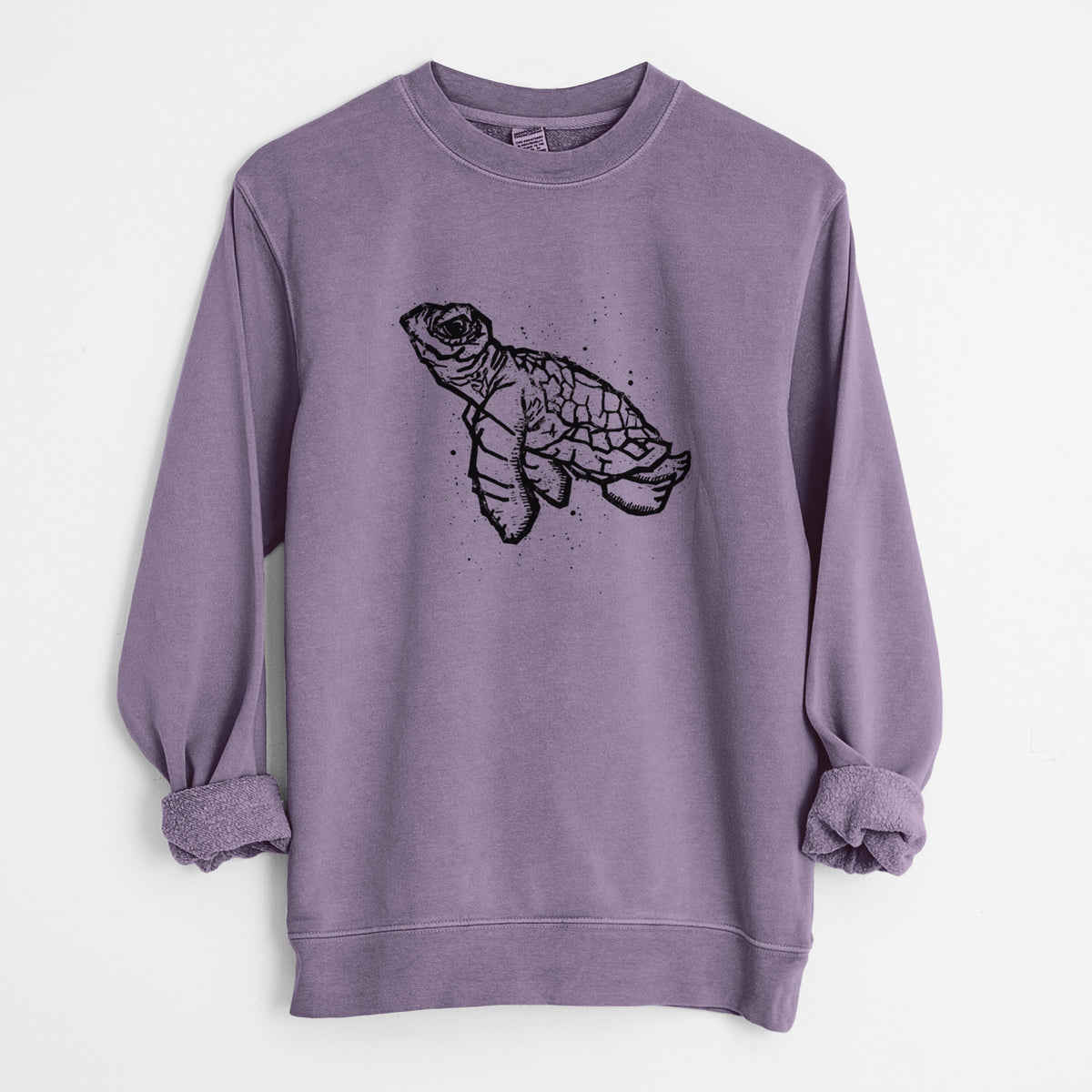 Plum purple pigment dyed crewneck sweatshirt laid flat with the sleeves rolled, printed with a black linocut-style illustration of a baby sea turtle with a patterned shell and ink splatters.