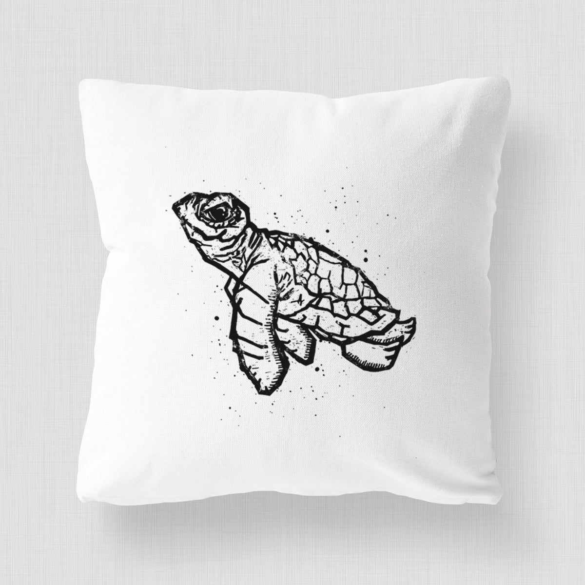 White pillow cover printed with a black linocut-style illustration of a baby sea turtle with a patterned shell and ink splatters.