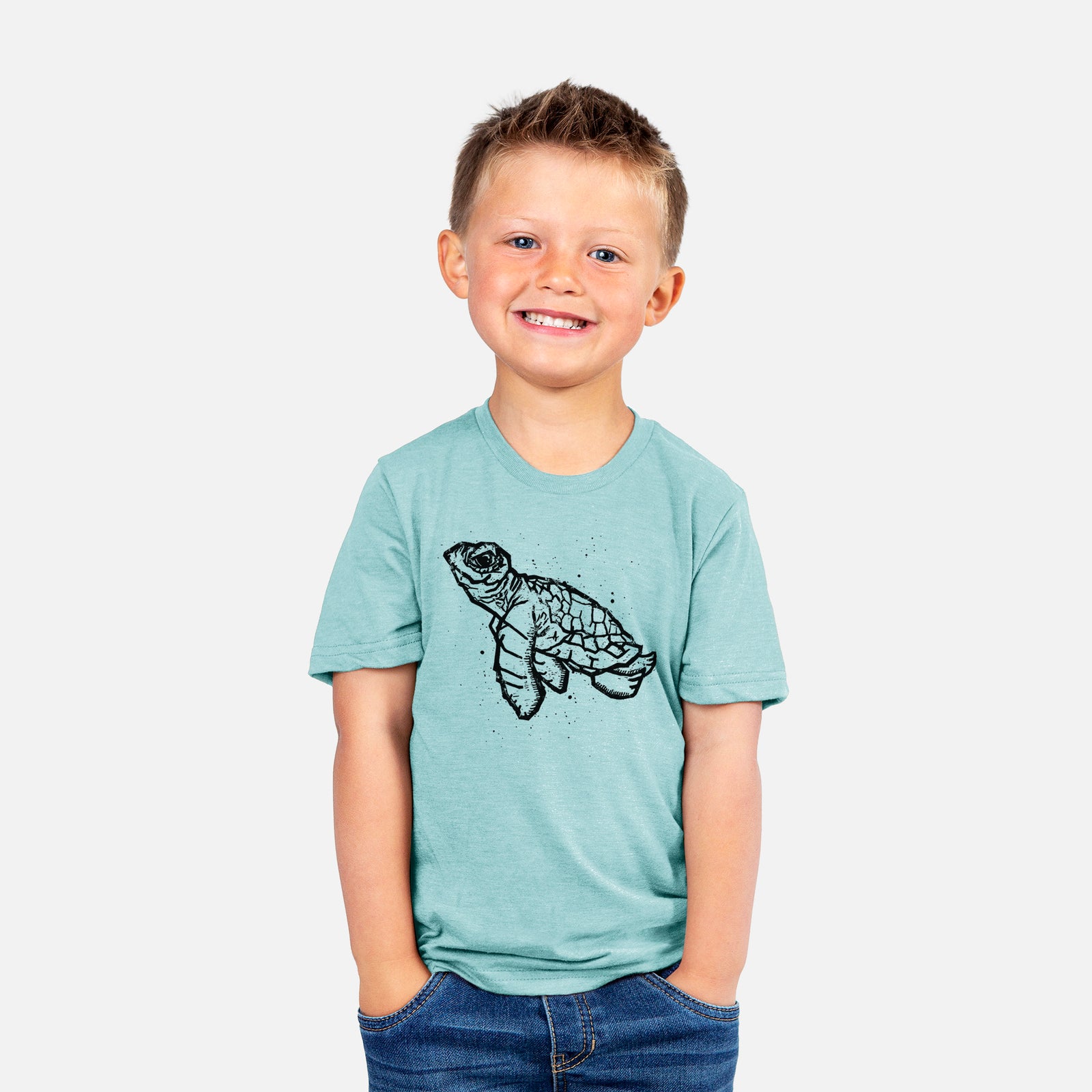 Two youth t-shirts in different colors on hangers, printed with a black linocut-style illustration of a baby sea turtle with a patterned shell and ink splatters.