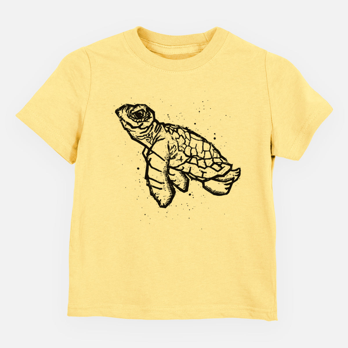 Butter yellow toddler t-shirt laid flat, printed with a black linocut-style illustration of a baby sea turtle with a patterned shell and ink splatters.